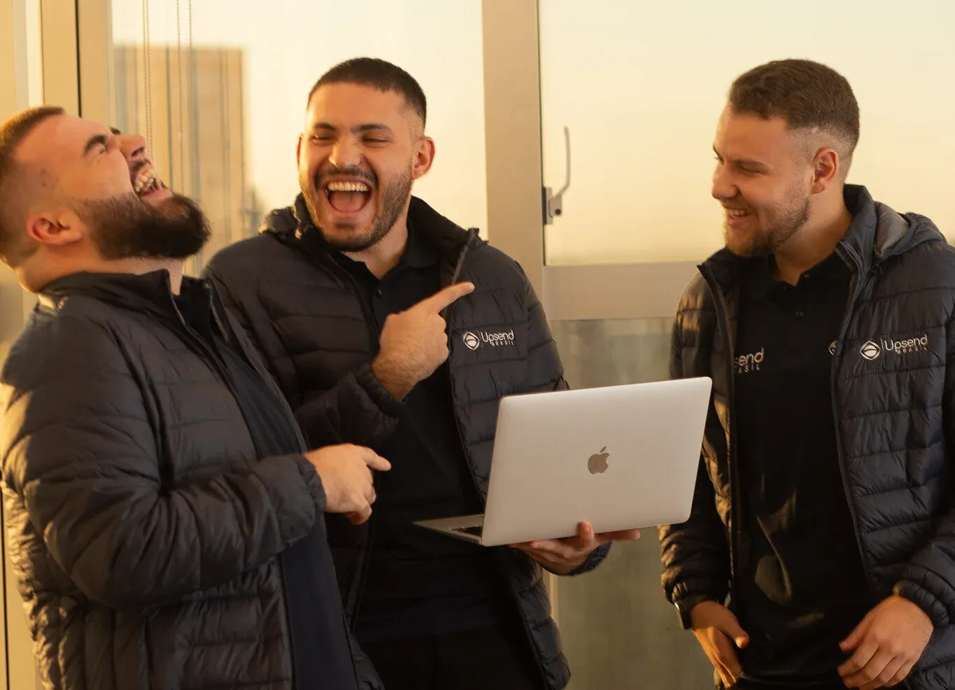 Sócios da Upsend Brasil conversando e rindo em volta de um notebook